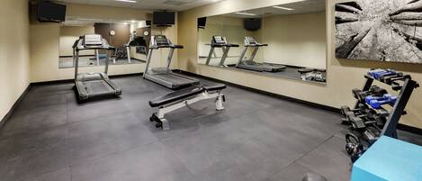 A gym with treadmills, weight benches, and a large mirror.