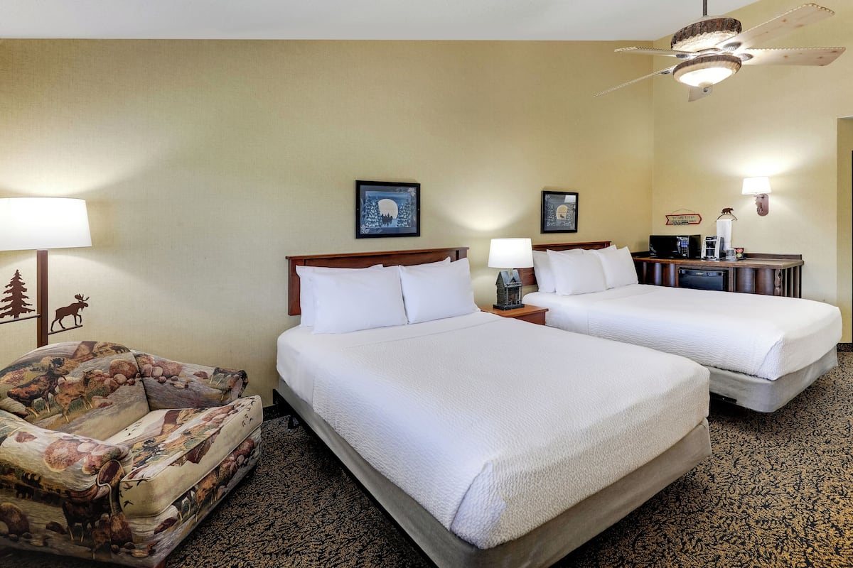 A hotel room with two beds, a sofa, a ceiling fan, and a wall-mounted lamp.