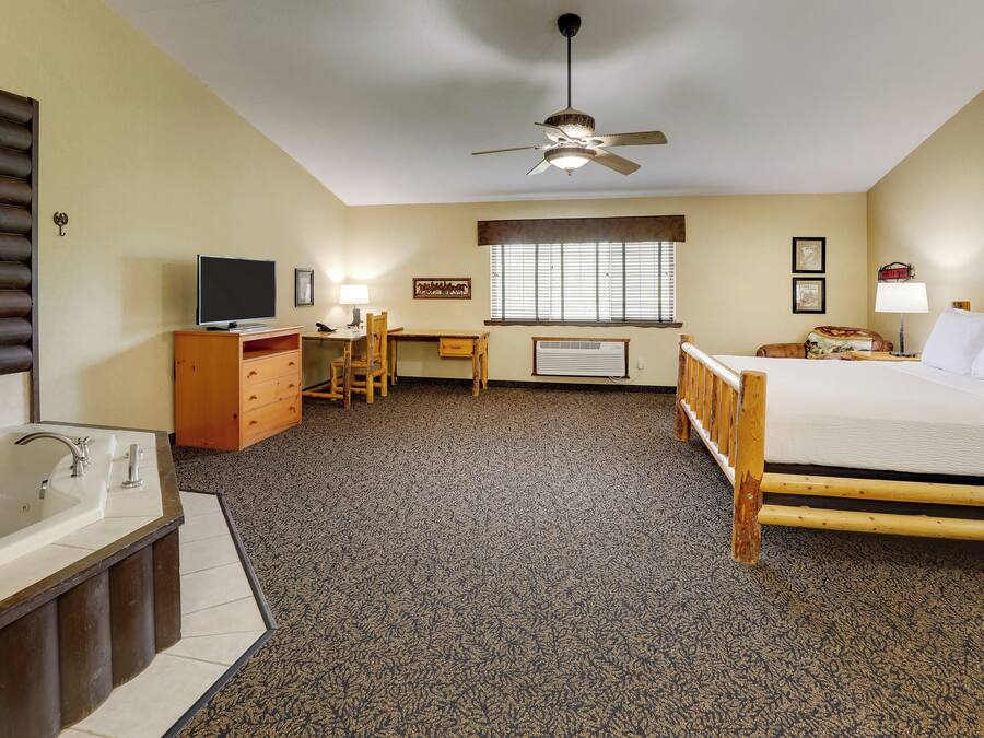A hotel room with a large bed, a desk, a chair, a television, a bathroom with a bathtub, and a ceiling fan.