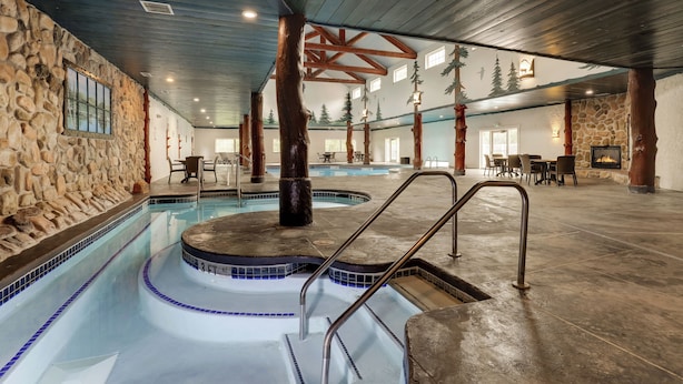 An indoor swimming pool with a stone wall, wooden beams, and a stone fireplace. - Stoney Creek Hotel La Crosse - Onalaska (Onalaska)