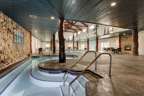 An indoor swimming pool with a stone wall, wooden beams, and a stone fireplace. - Stoney Creek Hotel La Crosse - Onalaska (Onalaska)