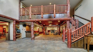 A spacious lobby with a stone floor, wooden staircase, and a second-floor balcony. - Stoney Creek Hotel La Crosse - Onalaska (Onalaska)