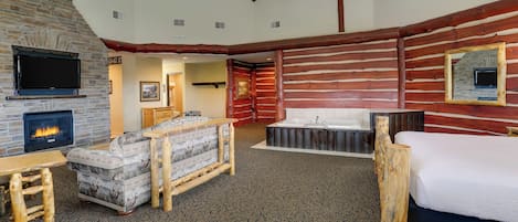 A log cabin-style room with a stone fireplace, a television, a sofa, a bed, and a bathtub.