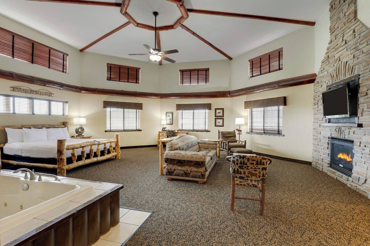 A spacious room with a large bed, a sitting area with a fireplace, and a ceiling fan.
