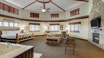 A spacious room with a large bed, a sitting area with a fireplace, and a ceiling fan.