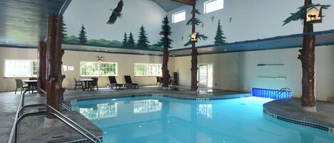 An indoor swimming pool with wooden beams, a mural of mountains and trees, and a lifeguard station.