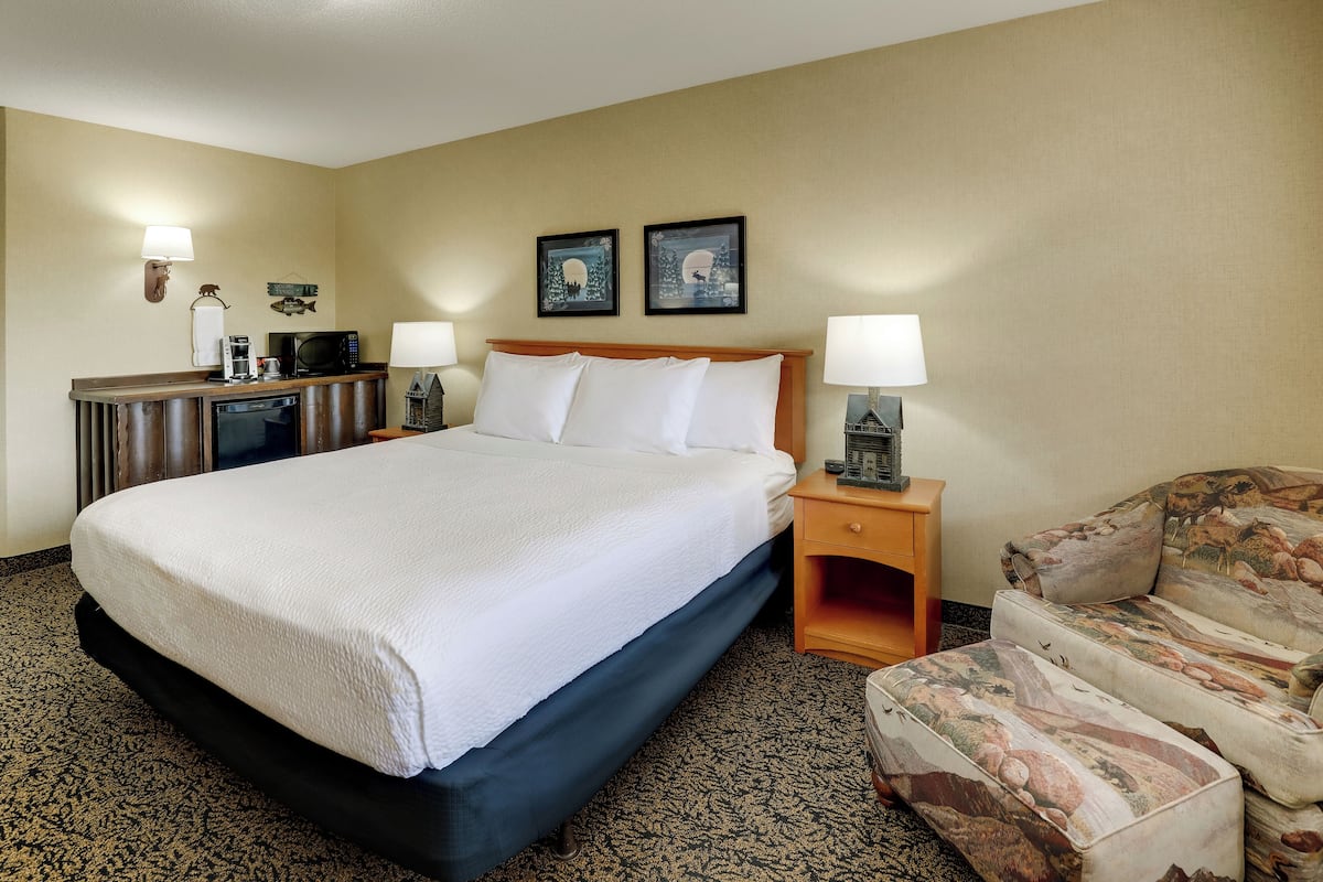 A hotel room with a large bed, a desk with a microwave, a chair, and two framed pictures on the wall.