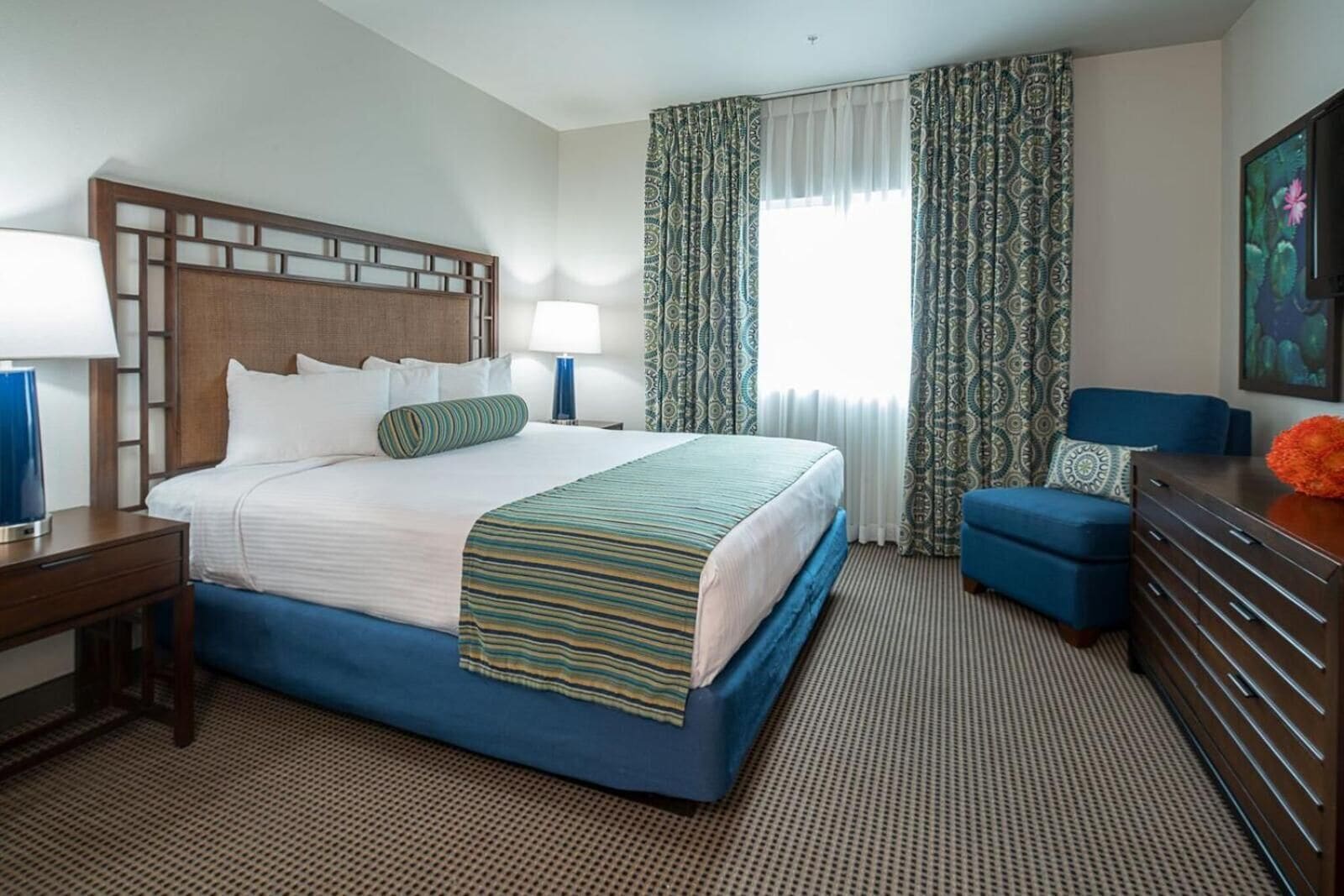 Une chambre d’hôtel avec un grand lit, un bureau, une commode et une fenêtre agrémentée de rideaux à motifs.