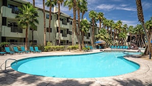 A swimming pool with lounge chairs and palm trees, surrounded by a multi-story building with balconies. - Tahiti Resort (Las Vegas)