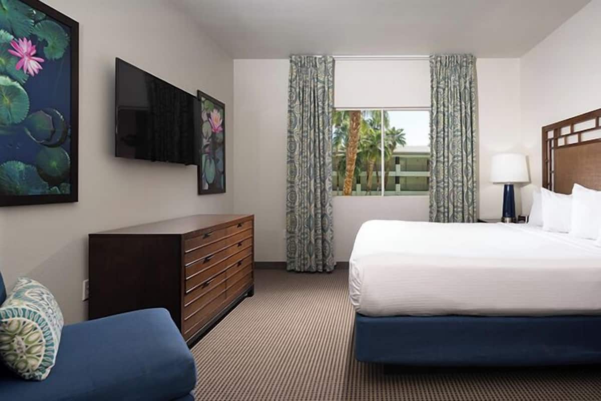 A hotel room with a large bed, a dresser, a television, and a window with curtains.