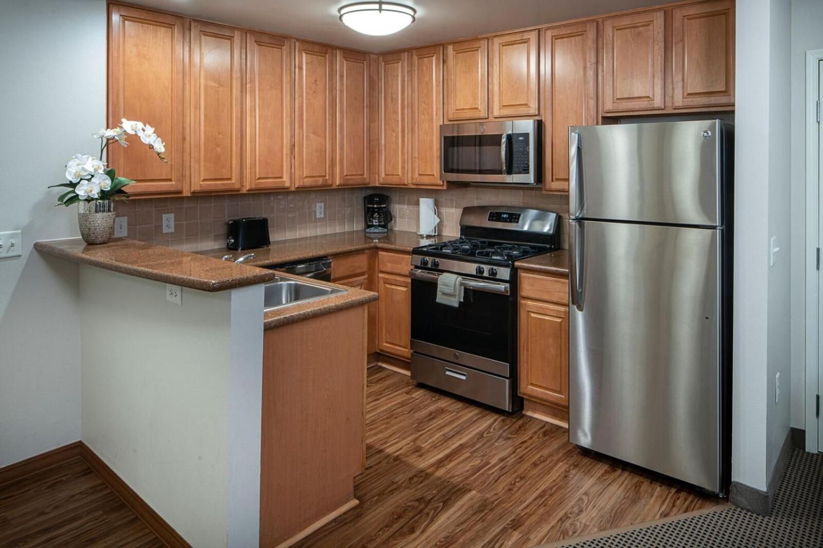 A kitchen with wooden cabinets, a stainless steel refrigerator, a microwave, a stove, and a sink.