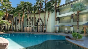 A swimming pool surrounded by palm trees and a multi-story building with balconies.