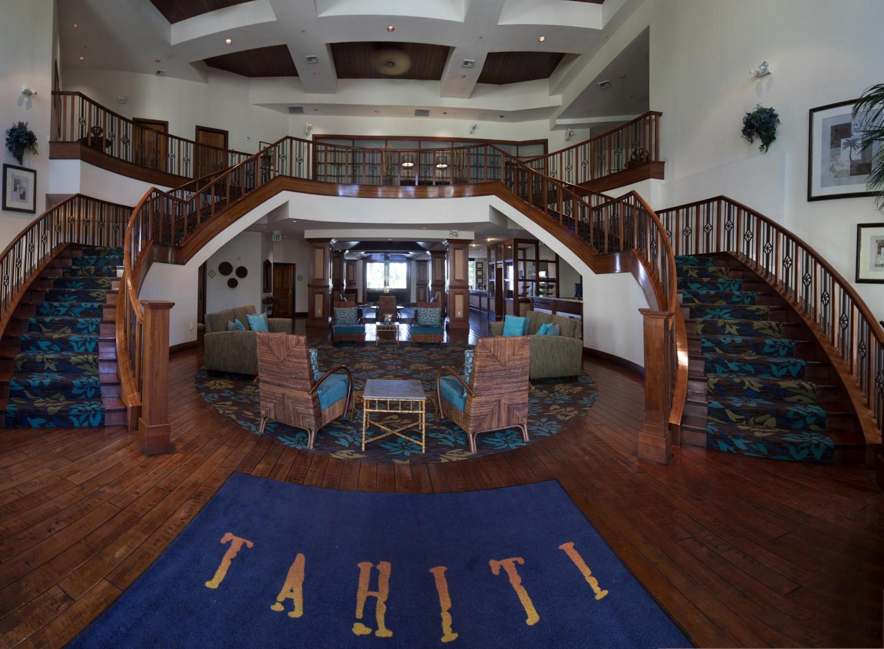 A spacious lobby with a central seating area, a grand staircase, and a view of the upper floor.