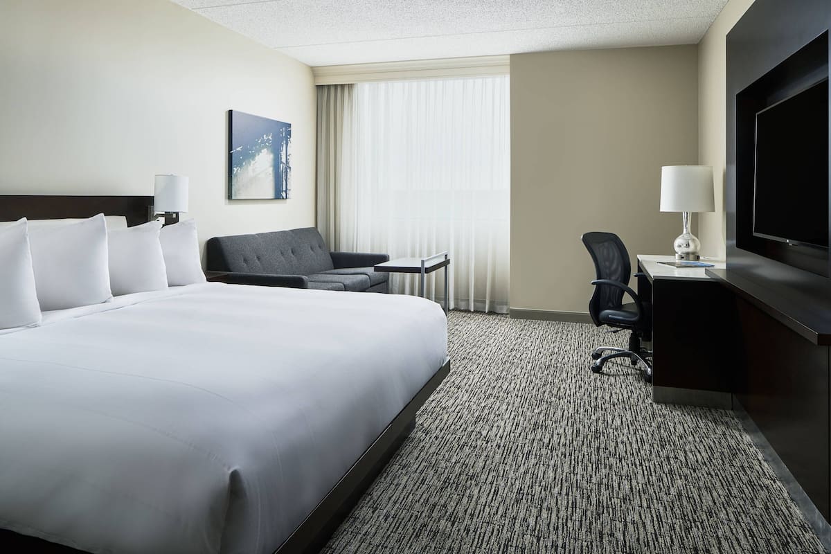 A hotel room with a large bed, a desk with a chair, a television, and a window with curtains.