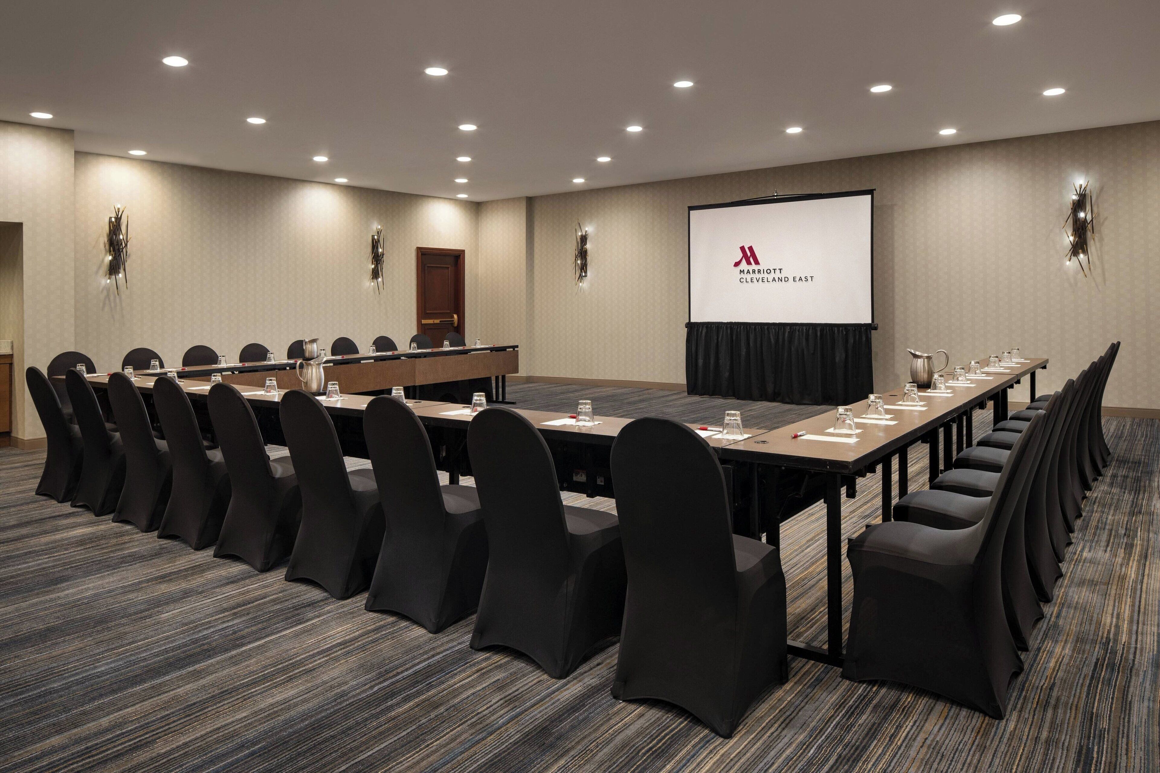 A conference room with a long table, black chairs, and a screen displaying the Marriott Cleveland logo.