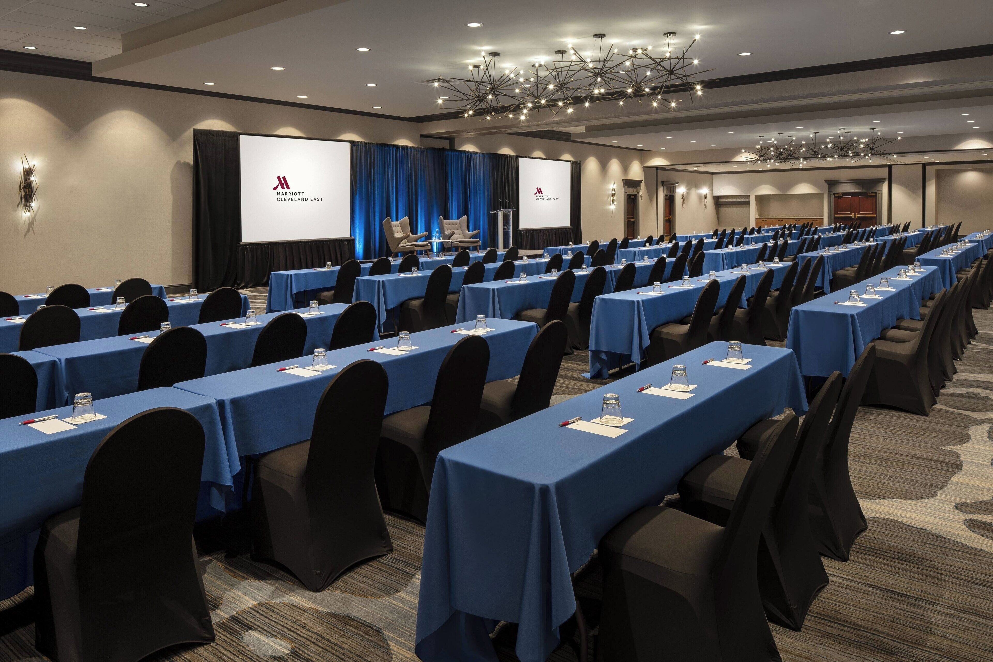 A conference room with rows of tables, blue tablecloths, and black chairs.