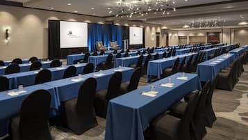 A conference room with rows of tables, blue tablecloths, and black chairs.