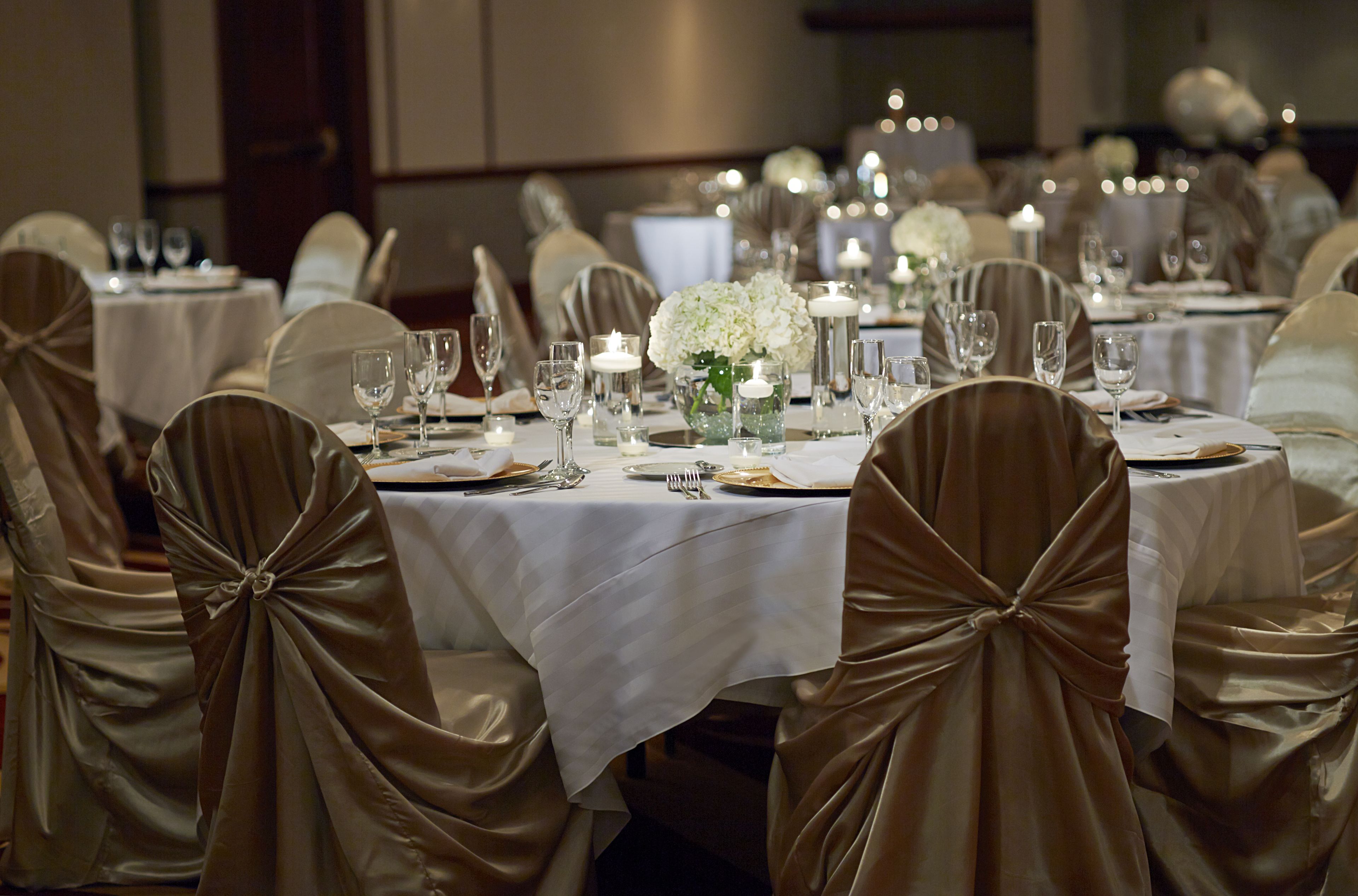 A banquet hall with round tables set for dining, each with white tablecloths and silverware.