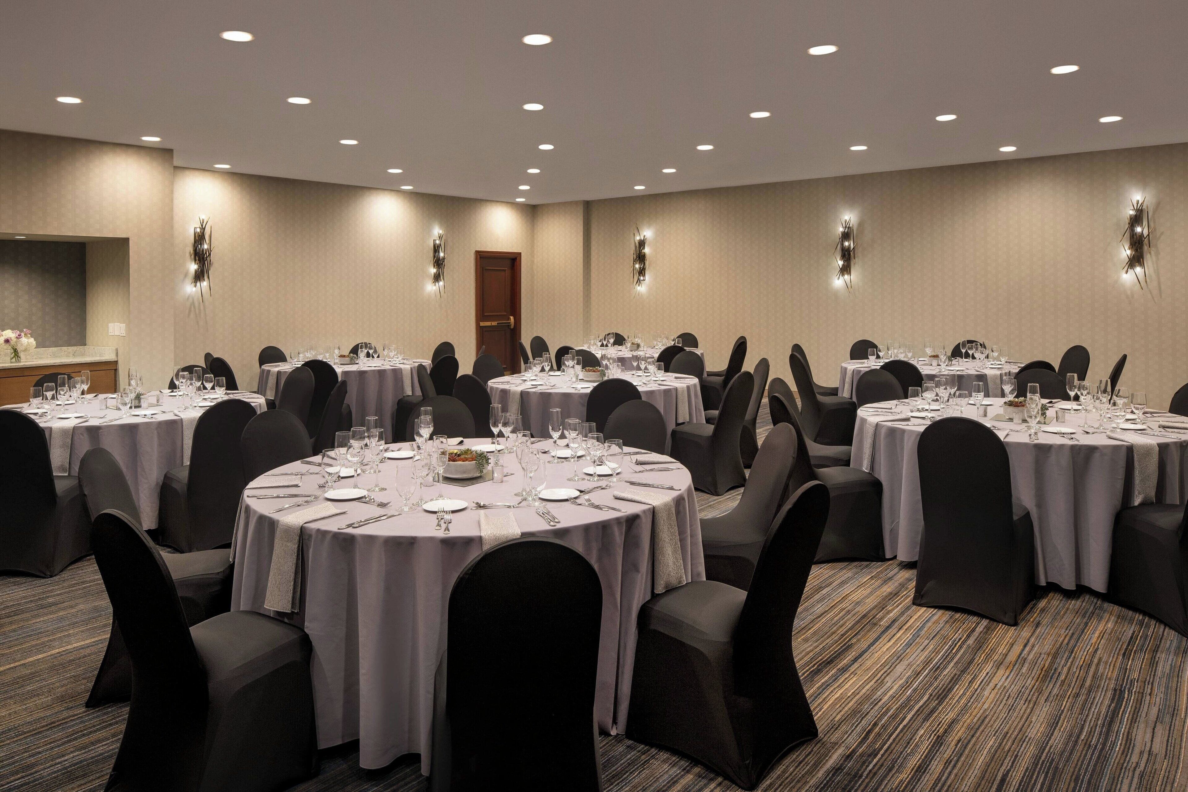 A conference room with multiple round tables, each set with plates, glasses, and cutlery.