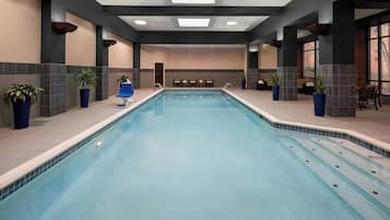 Une piscine intérieure à l’eau claire, entourée d’espaces aménagés pour s’asseoir et de plantes en pot.