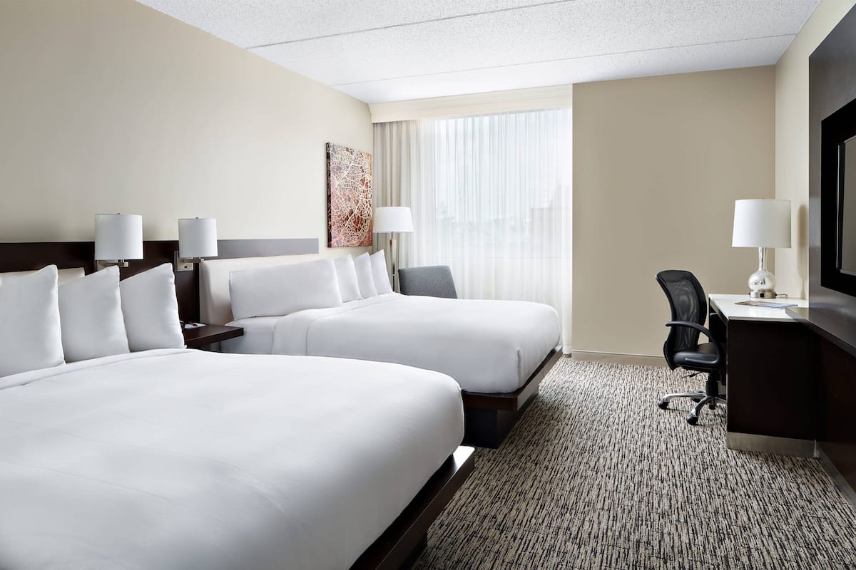 A hotel room with two beds, a desk, a chair, and a television.