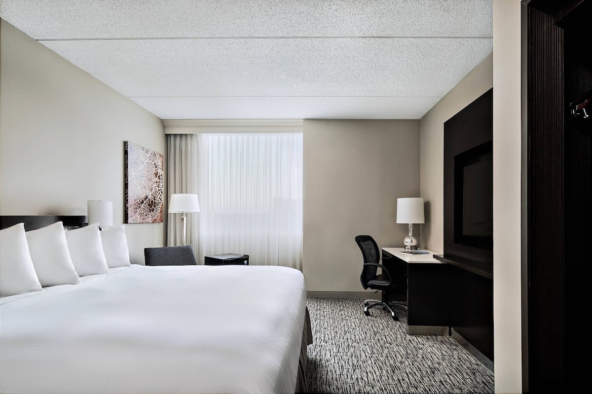 A hotel room with a large bed, a desk with a chair, a television, and a window with curtains.