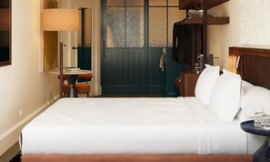 A hotel room with a bed, a desk, a chair, a lamp, and a wardrobe.