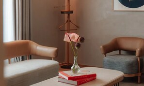 A room with two leather chairs, a small table with a vase of flowers and books, and a floor lamp.