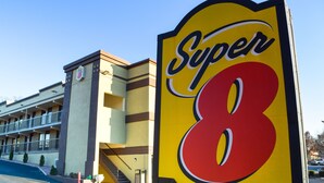 Een hotel met een opvallend 'Super 8' bord, een meerlaags gebouw met balkons en een parkeerplaats.