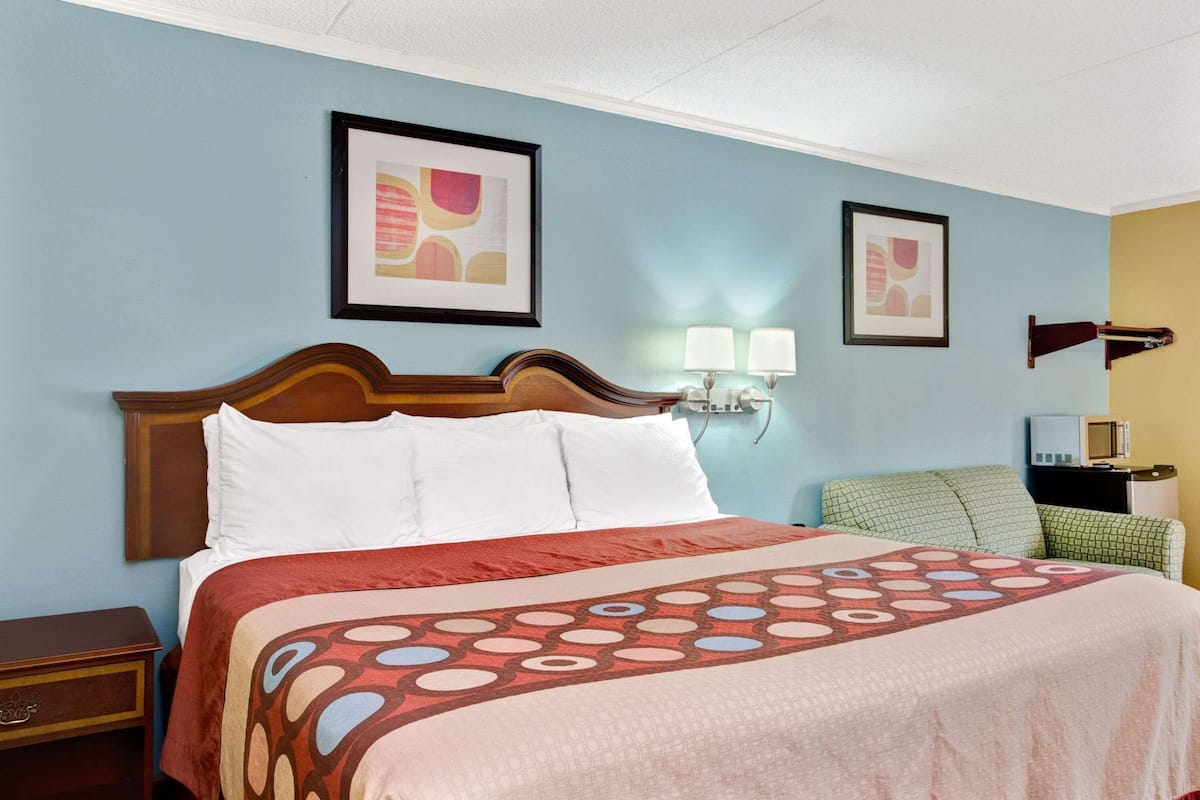 A hotel room with a bed, a nightstand, a lamp, a television, and two framed pictures on the wall.