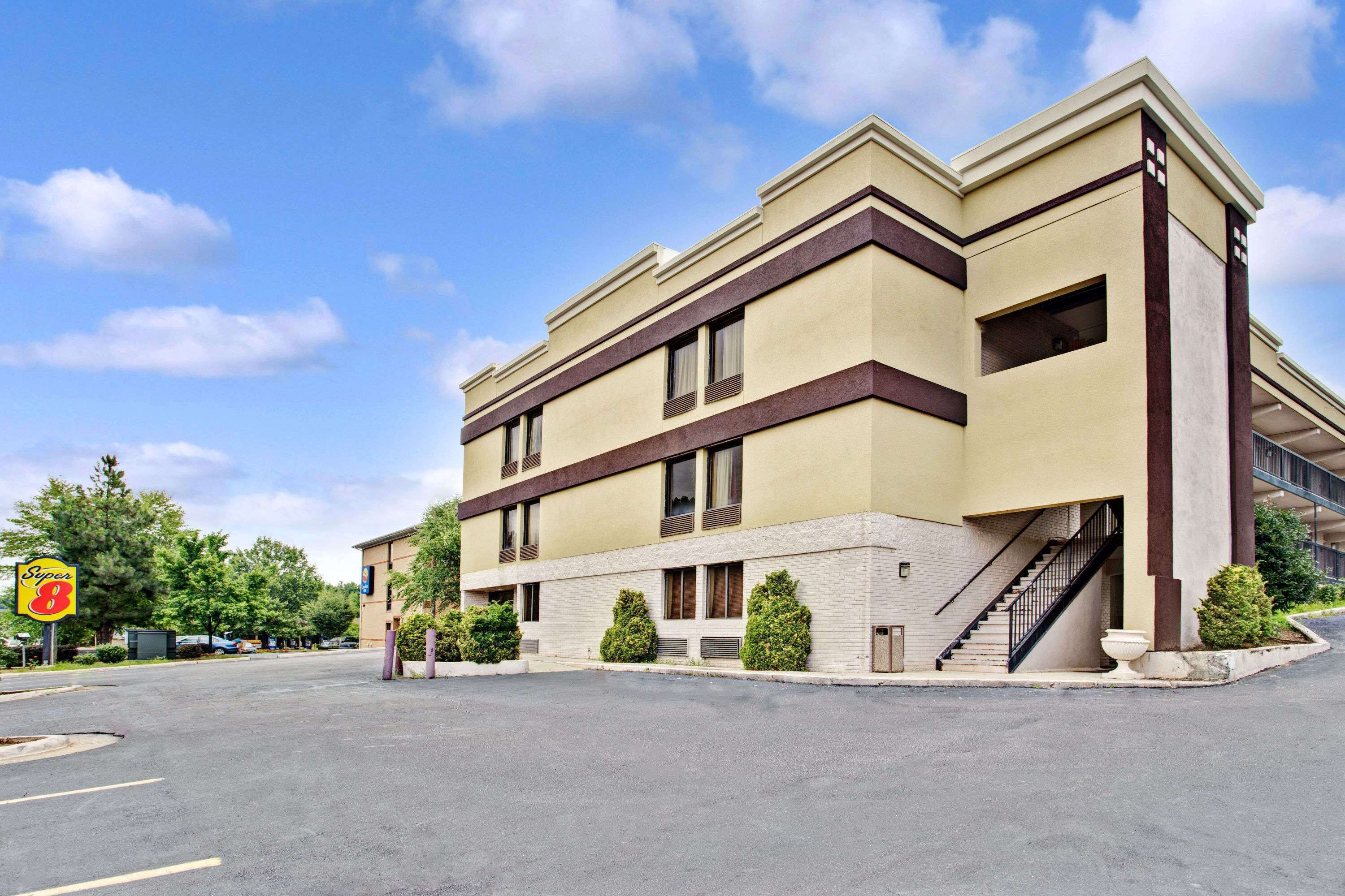 A multi-story hotel with a beige facade, a parking lot in front, and a visible staircase leading to the entrance.