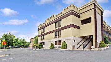 A multi-story hotel with a beige facade, a parking lot in front, and a visible staircase leading to the entrance.