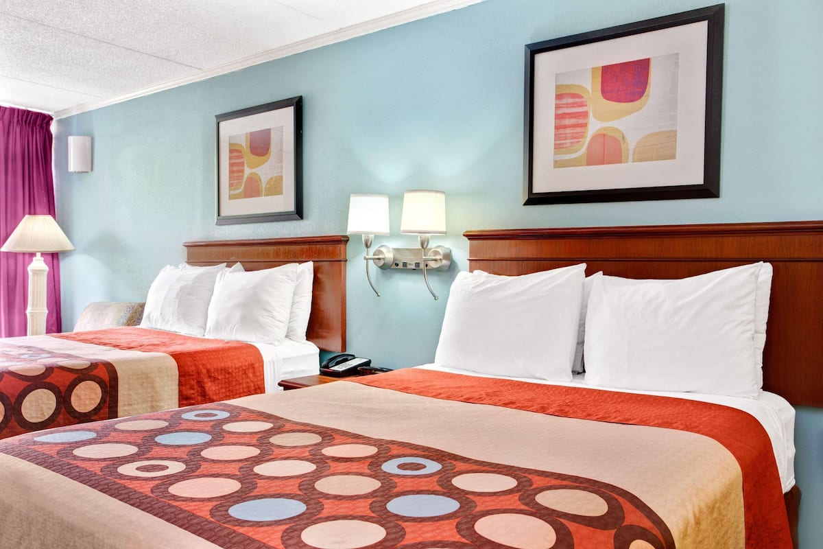A hotel room with two beds, a nightstand, a lamp, and wall-mounted lamps.