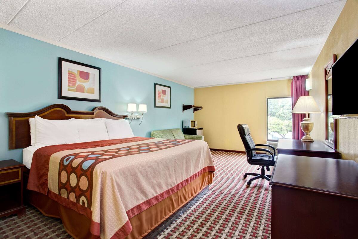 A hotel room with a bed, desk, chair, and artwork on the walls.