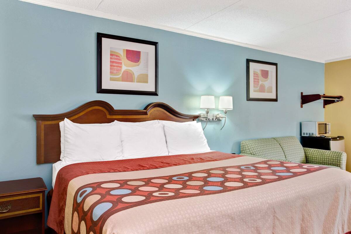 A hotel room with a large bed, two wall-mounted lamps, a television, and artwork on the walls.