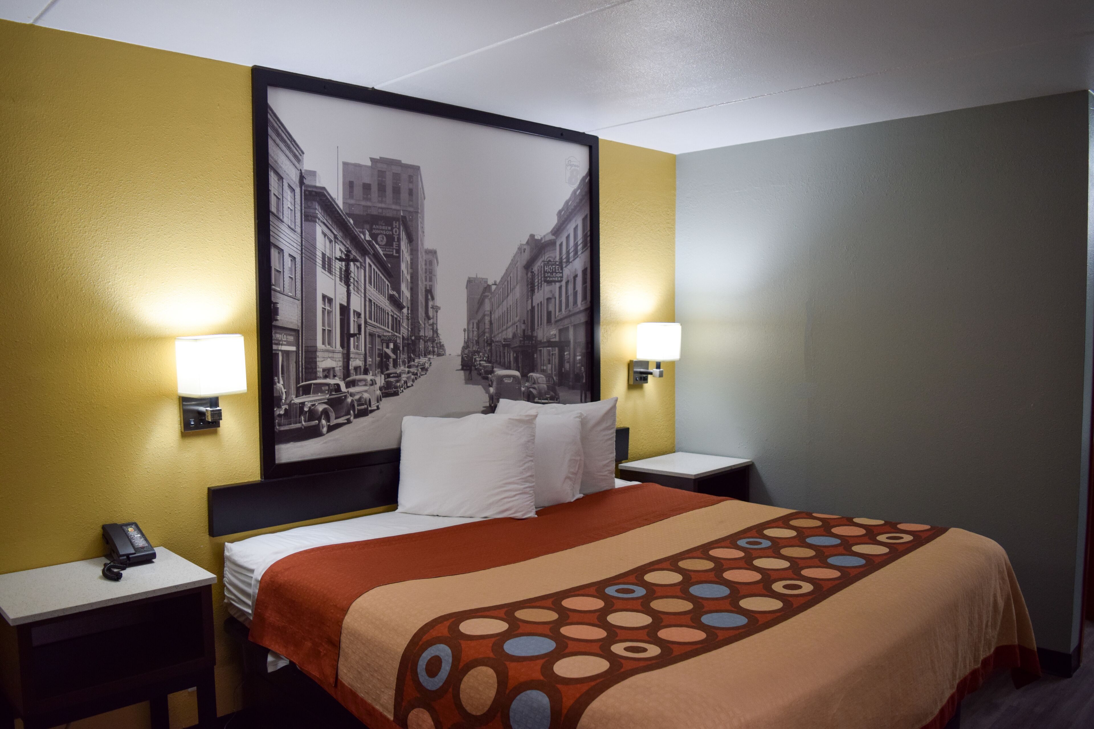 A hotel room with a bed, two bedside tables, a nightstand, a wall-mounted telephone, and two wall lamps.