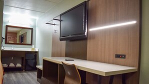 Hotelkamer met een flatscreen televisie aan de muur, een bureau met een stoel, een magnetron en een kleine koelkast.