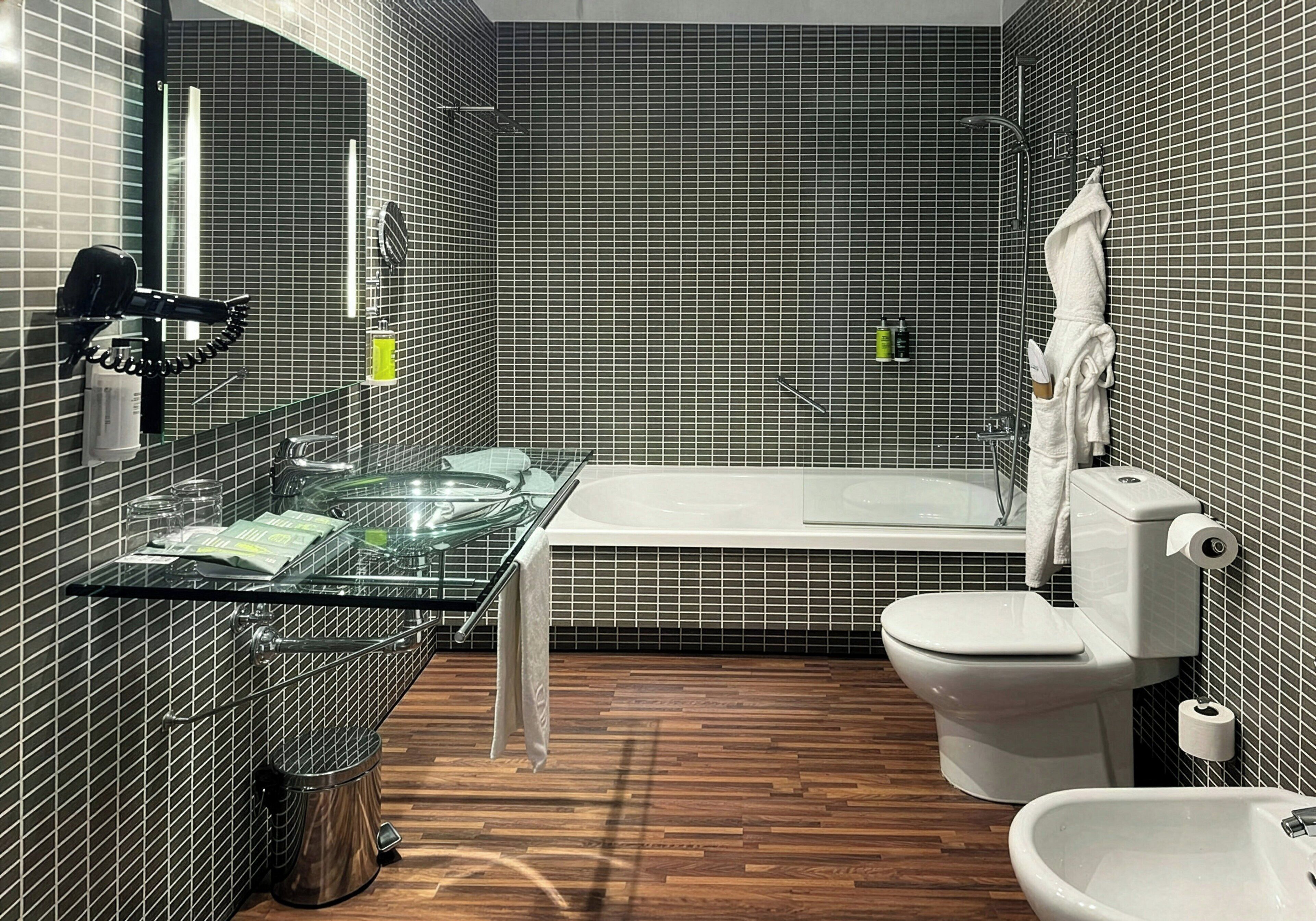 A bathroom with a glass shower enclosure, a white bathtub, a toilet, and a bidet.