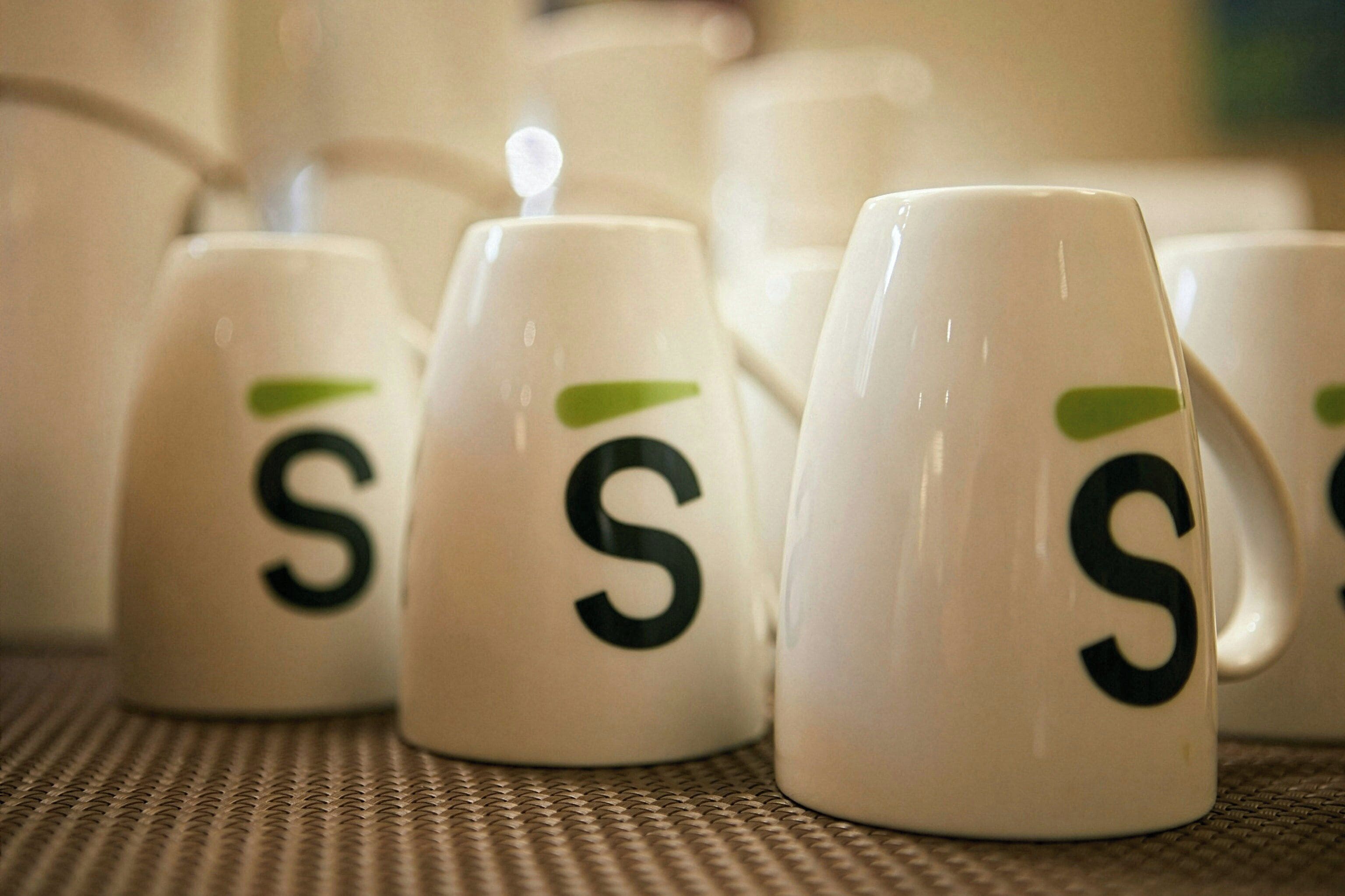 A row of white mugs with a green logo and the letter 'S' on them.