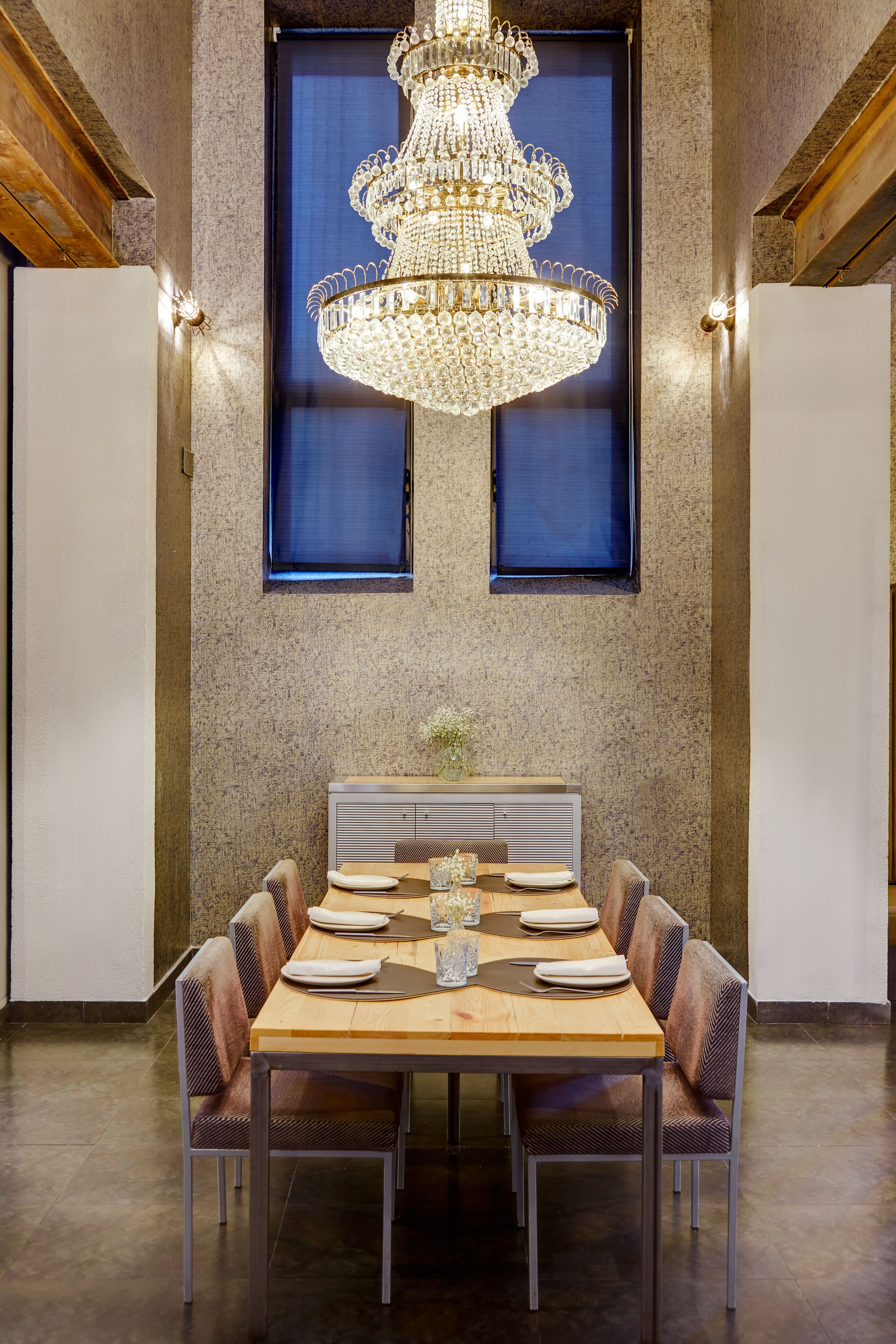 A dining area with a chandelier, two windows, and a table set for four.