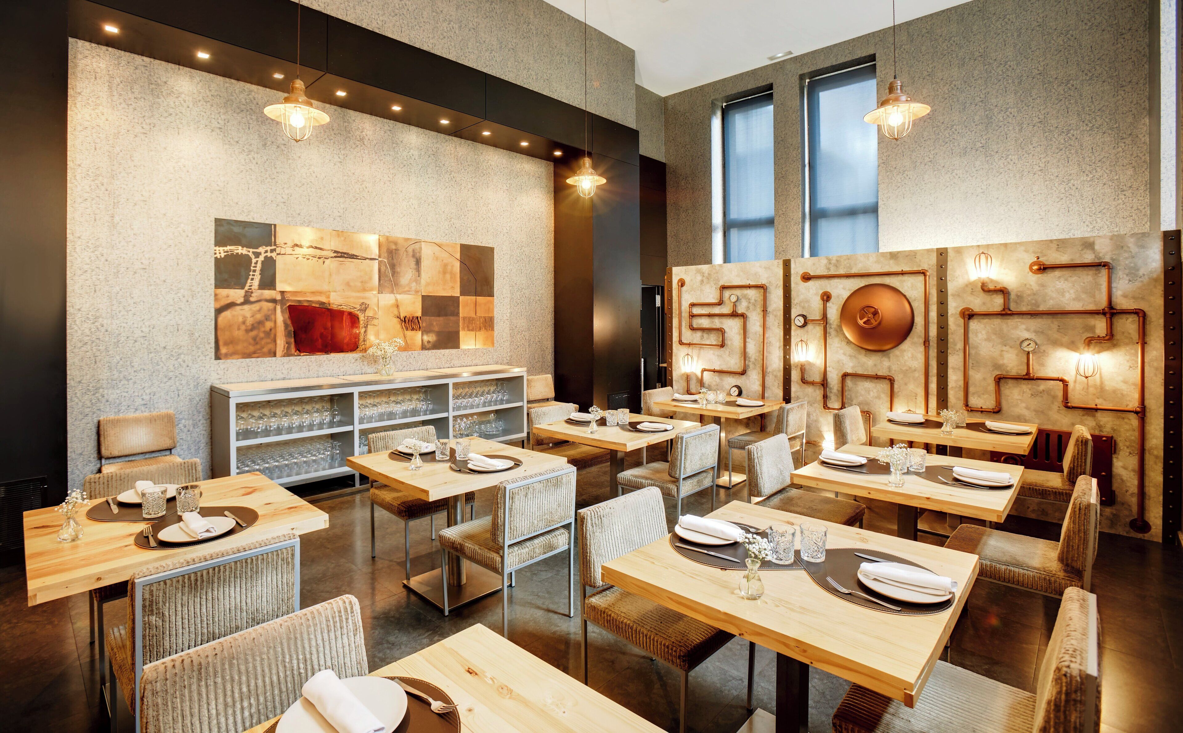 Een modern restaurant met houten tafels en stoelen, een groot abstract schilderij aan de muur en hangende lampen.