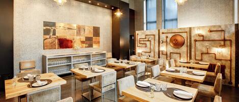 Un restaurante moderno con mesas y sillas de madera, un gran cuadro abstracto en la pared e iluminación colgante.
