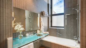 A modern bathroom with a glass countertop, a large mirror, a bathtub, and a shower area.