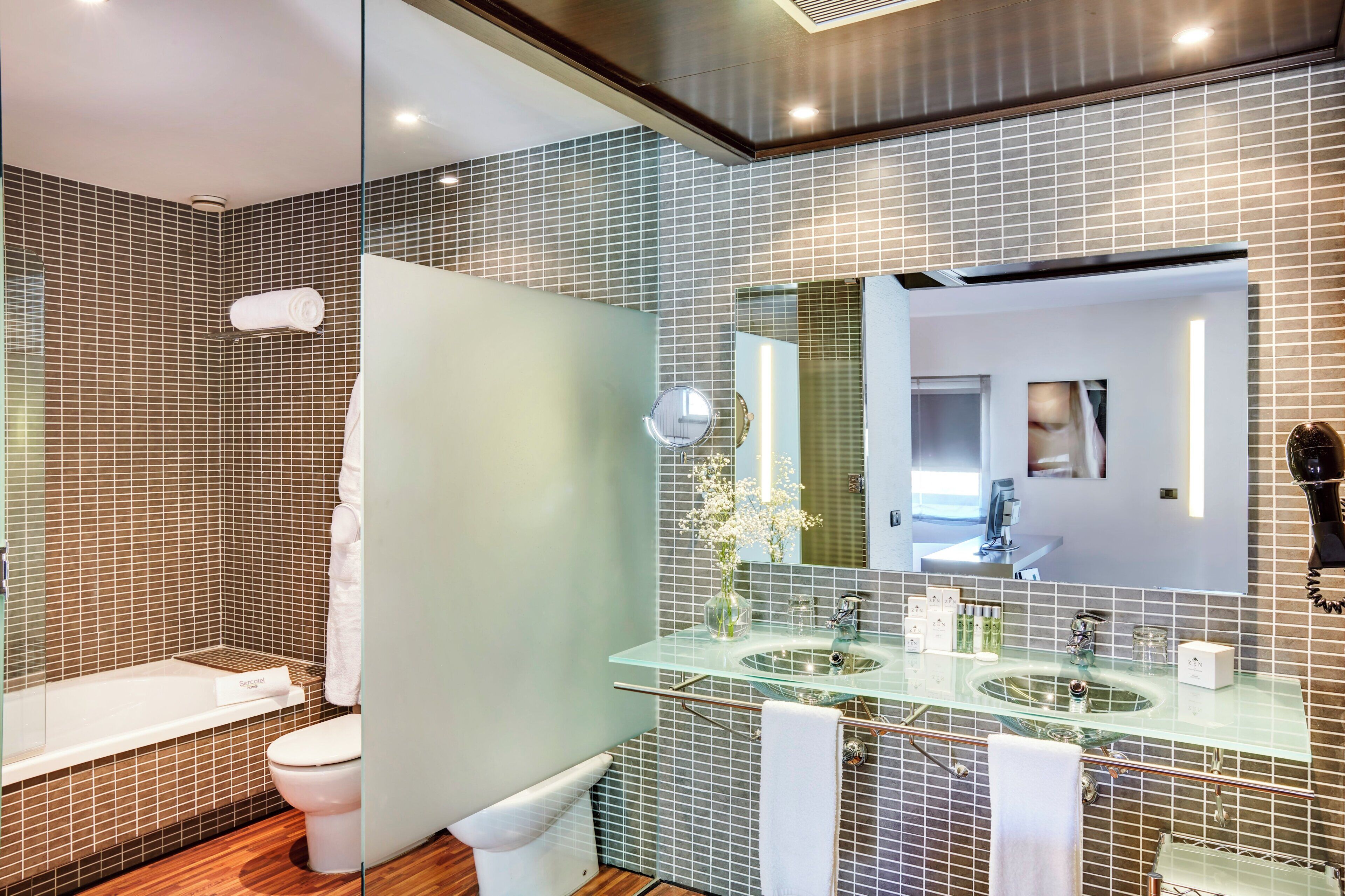 A modern bathroom with a glass sink, a large mirror, and a shower area.