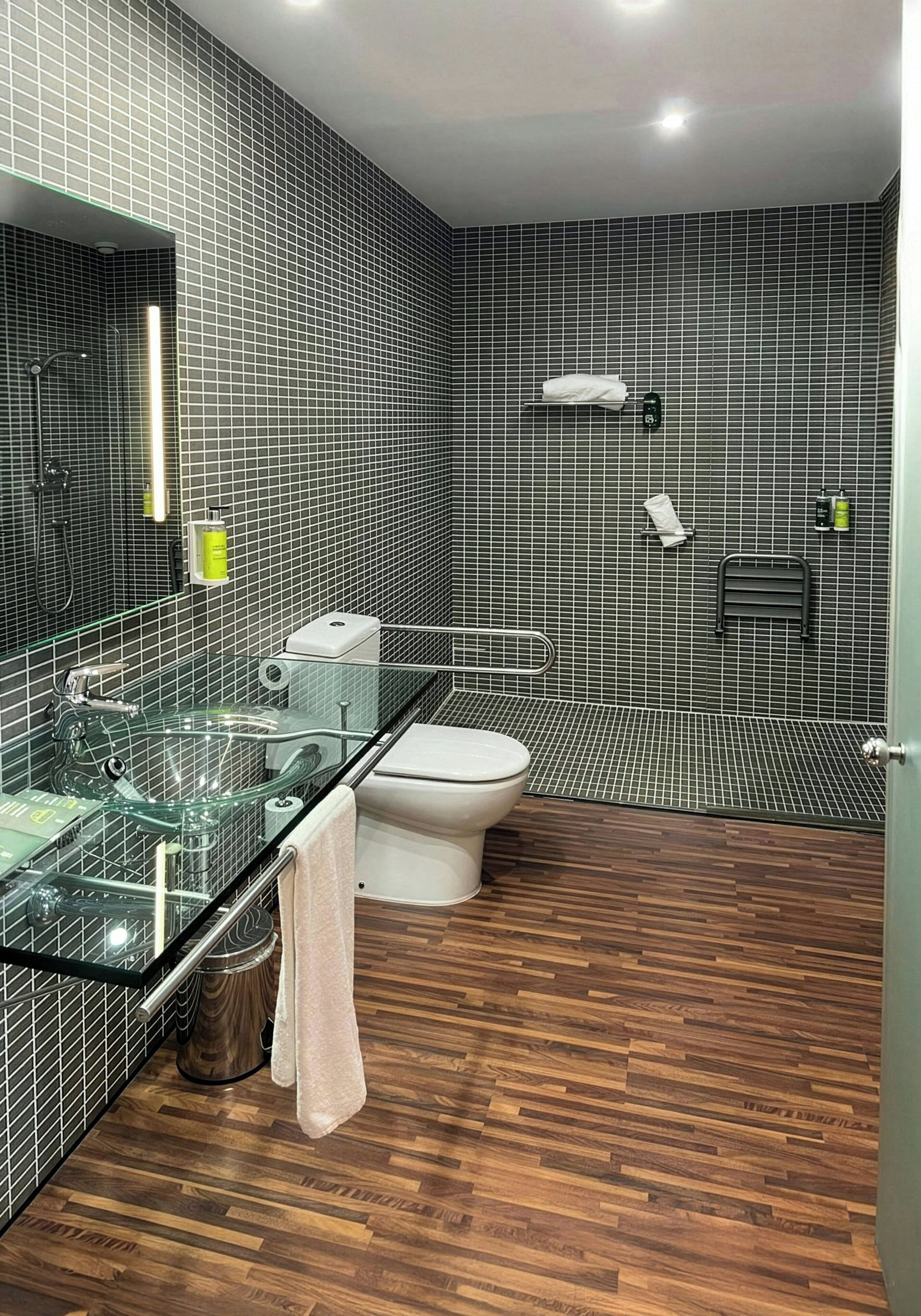 A modern bathroom with a glass shower enclosure, a white toilet, and a wooden floor.