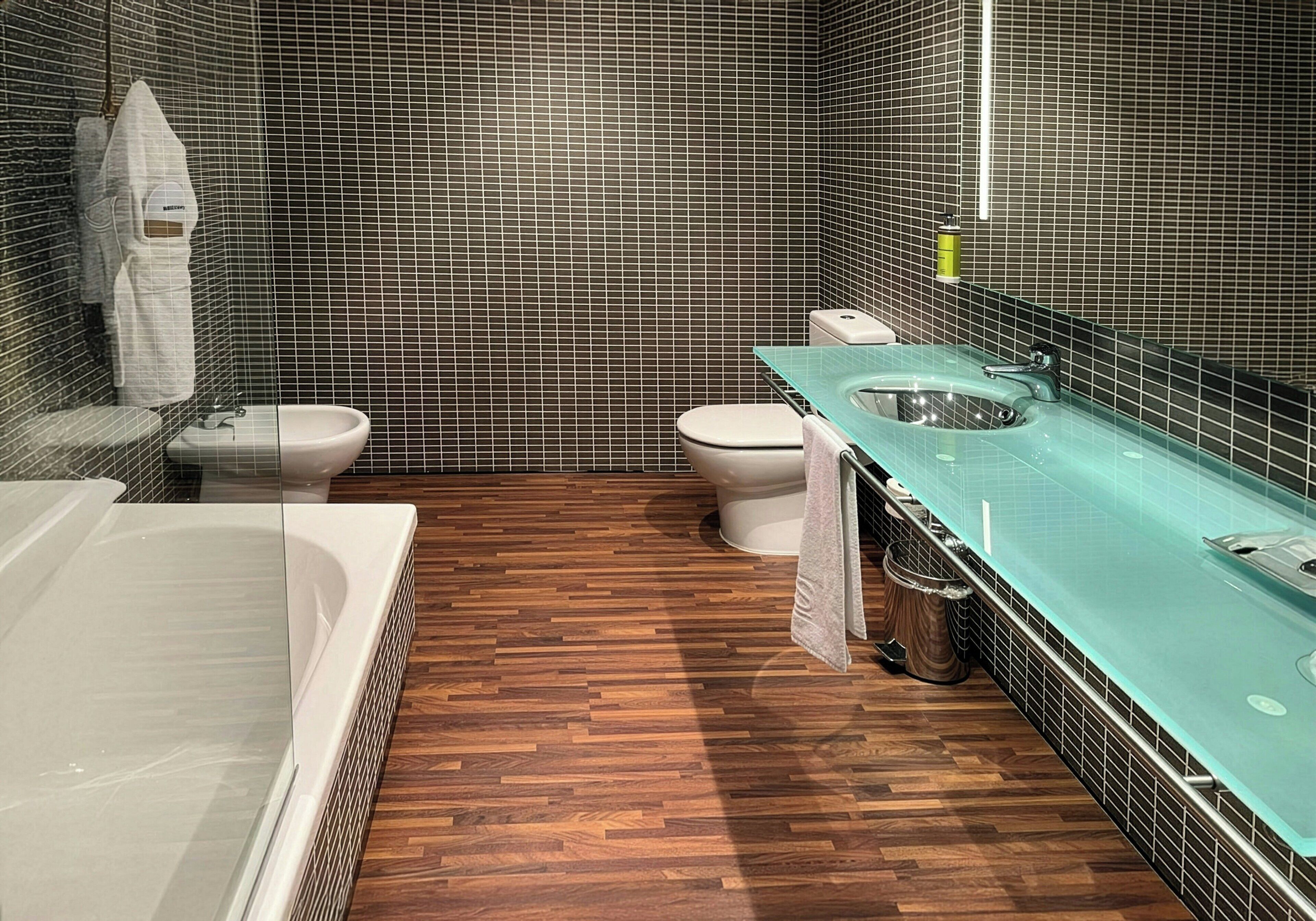 A modern bathroom with a glass sink, a bathtub, and a toilet.
