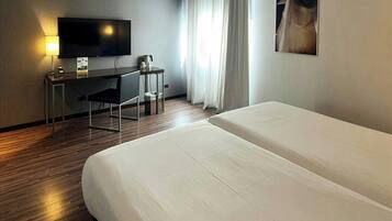 Habitación de hotel con cama, escritorio con televisor, cafetera y ventana con cortinas.