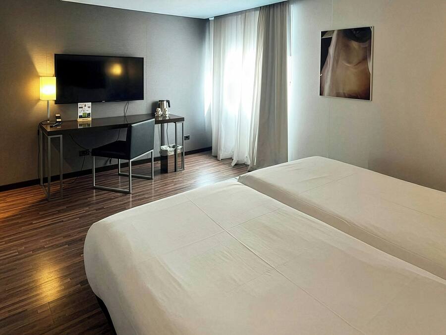 A hotel room with a bed, a desk with a TV, a coffee maker, and a window with curtains.