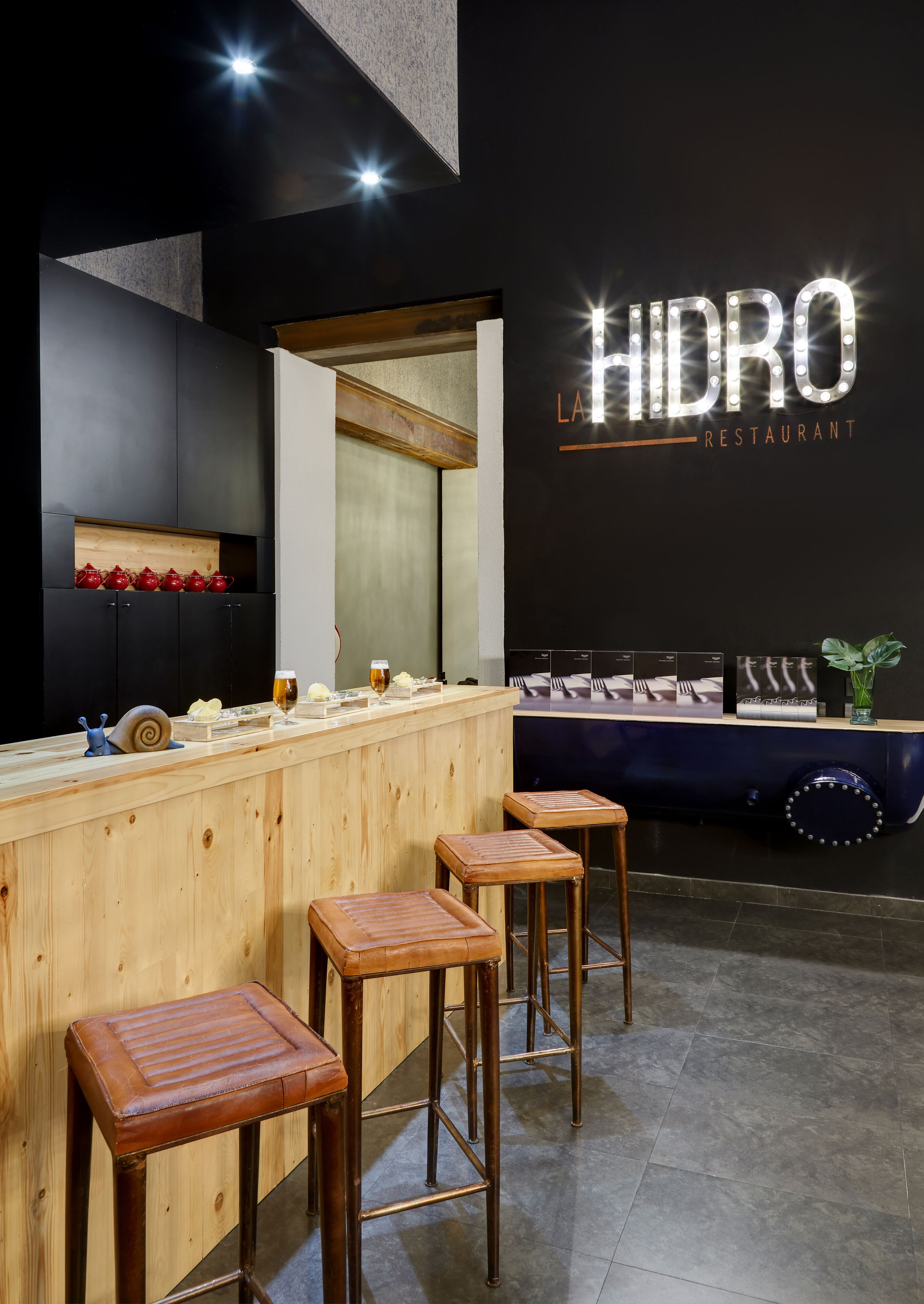 Een bar met krukken, een houten toonbank en een muur met de tekst 'LA HIDRO RESTAURANT'.