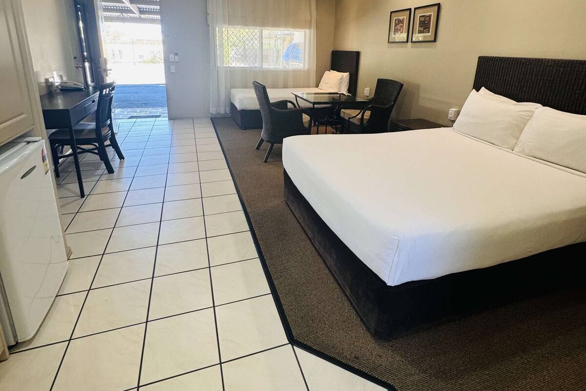 Habitación de hotel con una cama grande, un escritorio con silla, una mesita y un refrigerador.